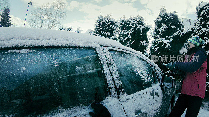 女司机刮着白雪覆盖的车窗