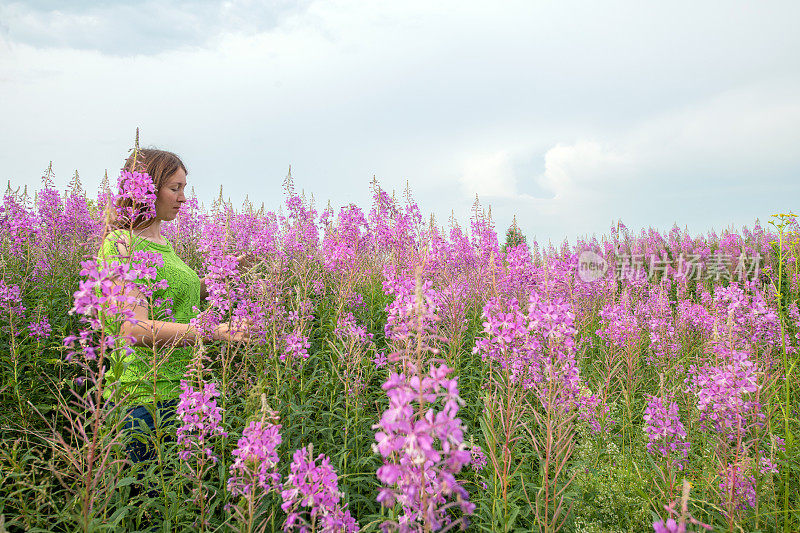 俄罗斯乌拉尔地区，站在鲜花盛开的杂草地里的绿衣女子