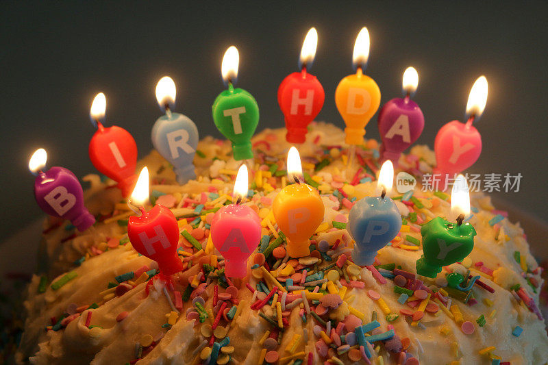 家庭制作的生日蛋糕的形象与多色点燃蜡烛拼写生日快乐，庆祝蛋糕覆盖白色奶油和糖果糊，照亮蜡烛火焰