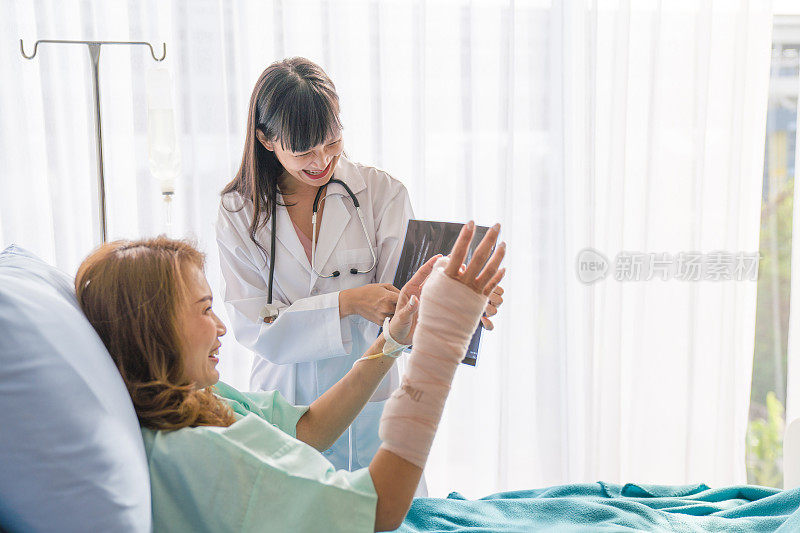 在医院里，坐在轮椅上的病人，专业的医生在为女性折叠的骨折手臂和包扎的手解读x光图像