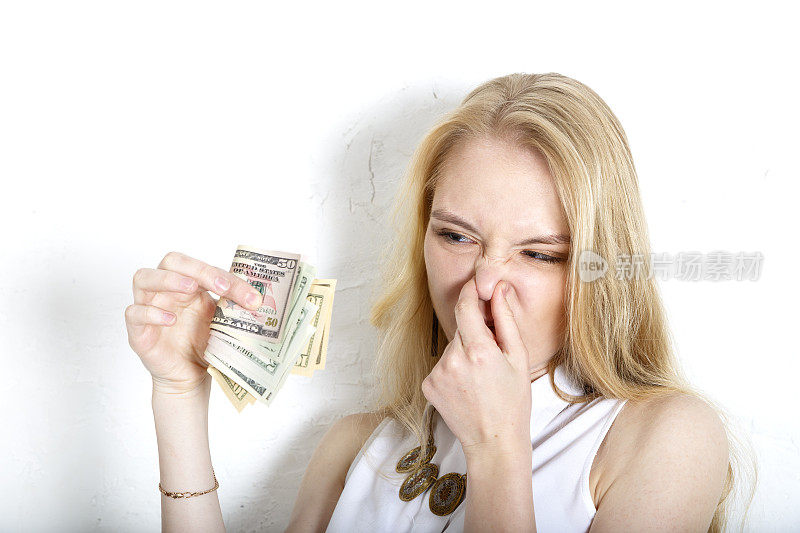 金发女郎用手指挤了挤鼻子，闻到了美钞的味道。脏钱的概念。