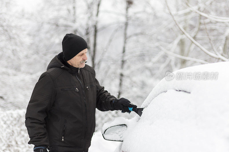 成熟的男人清理车上的雪