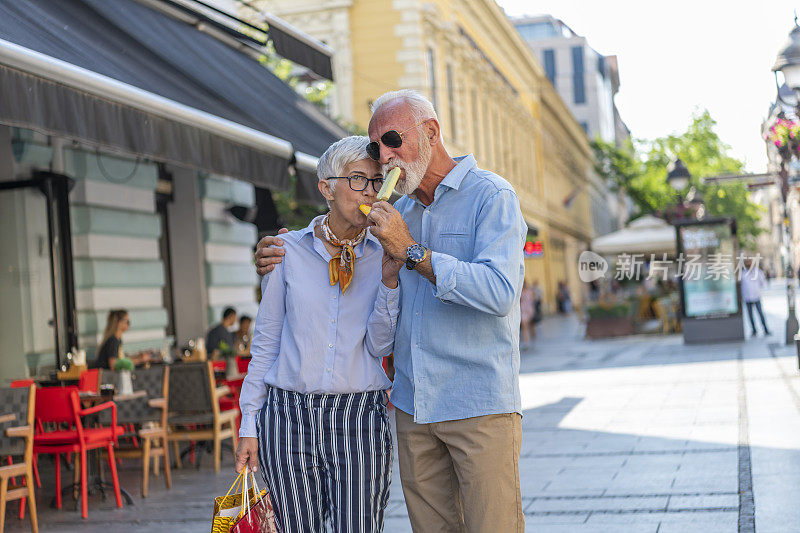 老英俊的胡子男人正与他的妻子散步，享受着冰激淋