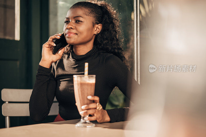 一个黑人妇女独自坐在路边的咖啡馆里，正在打手机