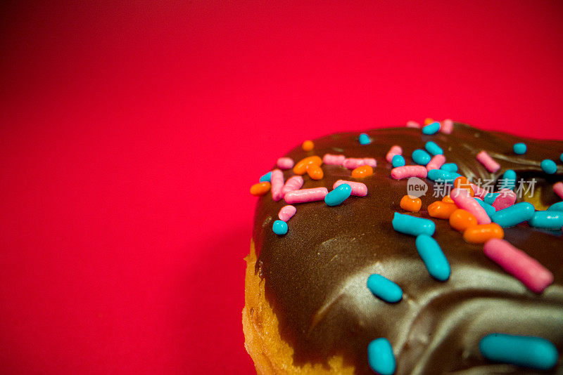 极近距离拍摄的巧克力釉酵母凸起的甜甜圈与点缀在明亮的红色无缝背景