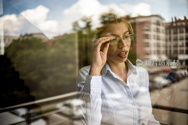 一位女商人站在窗边，一边思考一边谈生意