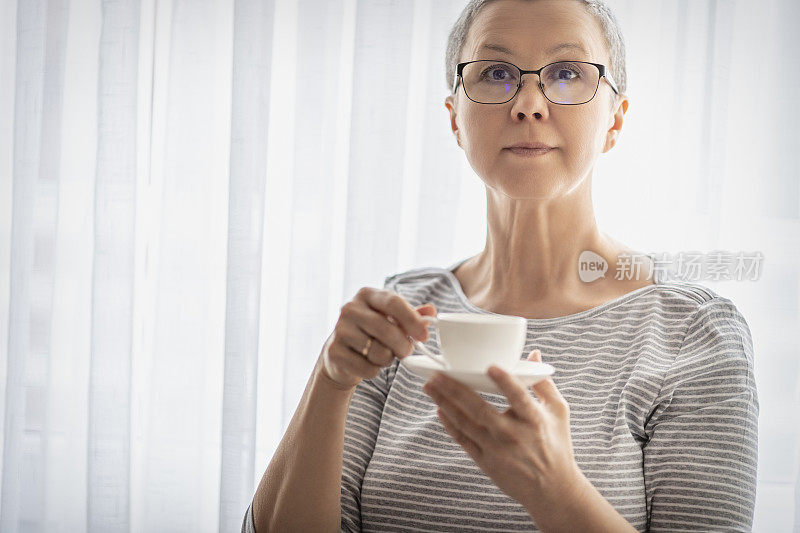 一个站在窗边喝着咖啡的成熟女人