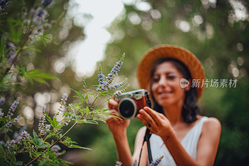 身穿白裙、头戴草帽的女子用老式相机拍自然照片