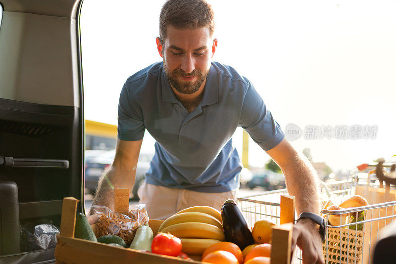 年轻人把装着水果和蔬菜的盒子装进汽车后备箱