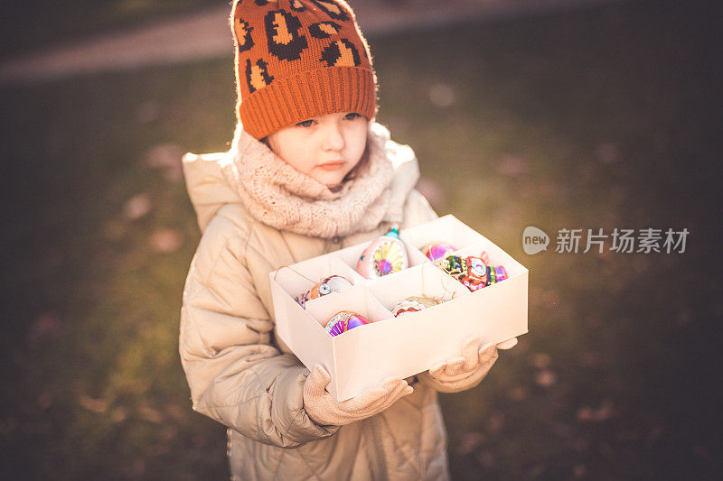 一个学龄前的小女孩手里拿着盒子里的圣诞装饰品