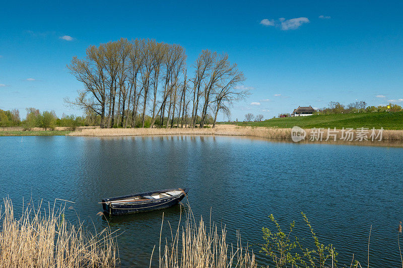 荷兰的河流景观。前景是一艘划艇。远处是河堤和一座白色的农场。
