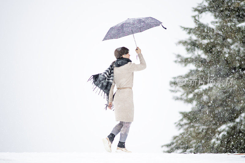 一个模模糊糊的女人撑着伞，下着雪，前面是一片森林