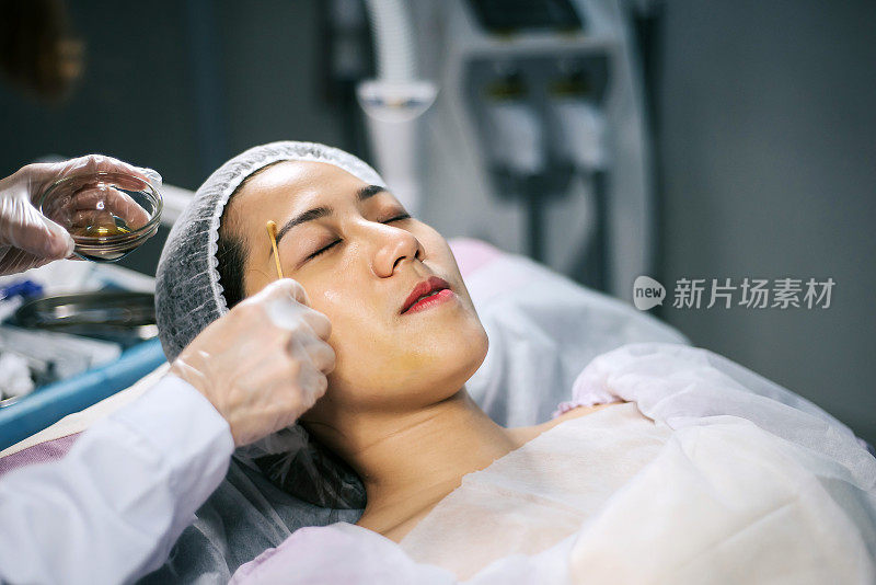 亚洲华人女性美容师在手术室手术前用棉签清洁她的客户的脸