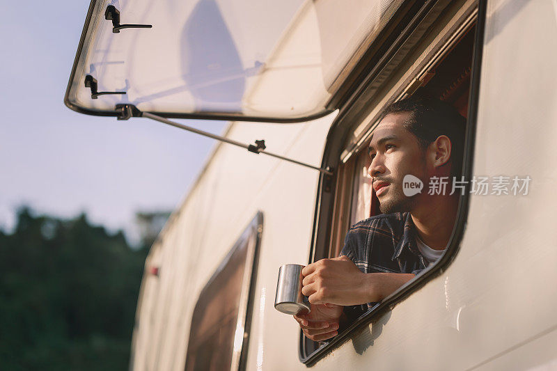 英俊的年轻亚洲男子，在公路旅行，坐在露营车里在早上。舒适的设置在露营拖车或货车。21、千禧年旅行潮流，冒险路上行