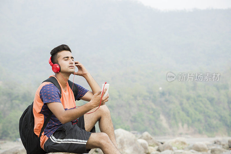 年轻人听音乐坐在岩石在山车站:-库存照片