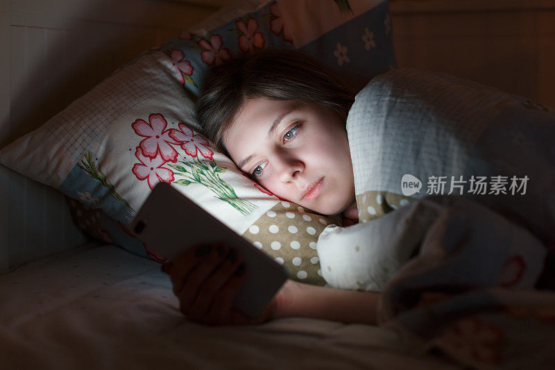 年轻困倦的女孩躺在床上玩智能手机到深夜