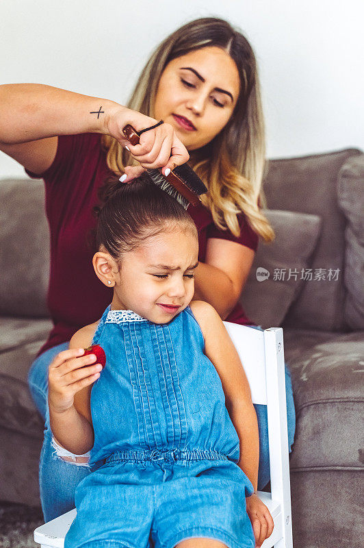 妈妈在家里梳着一个很不开心的小女孩的头发，家庭主妇的生活