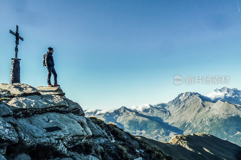 一个人站在山顶的侧面，身后有一座十字架纪念碑