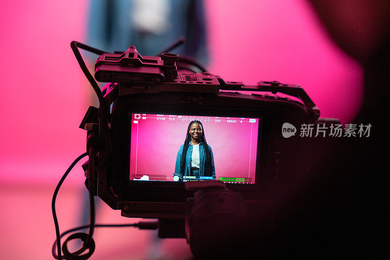 一个年轻的博主在一个粉红色背景的屏幕上，摄像机的前景