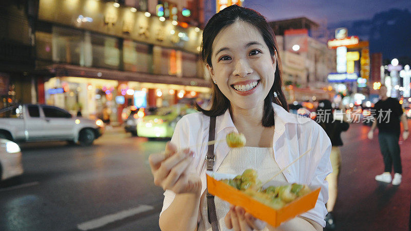 站在当地街头的亚洲妇女在街头夜市享受着当地传统的泰国食物Patongo