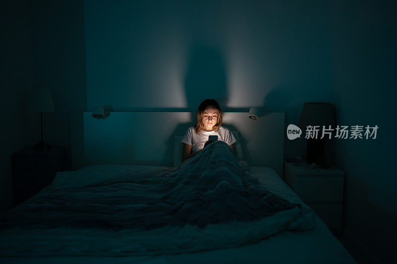 困倦的女人深夜躺在床上用智能手机，睡不着。失眠、成瘾概念