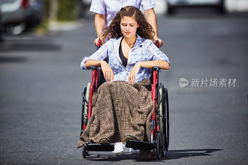 悲伤的卷发年轻女子坐在轮椅上，由身穿白色制服的护士推着