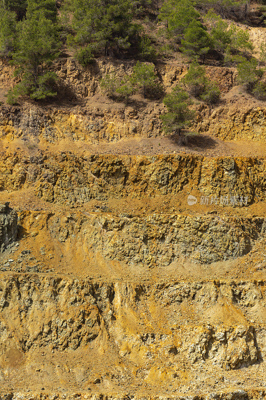 彩色的阶梯式斜坡，废弃的露天矿山，含硫的碎石和稀疏的树木在框架的顶部