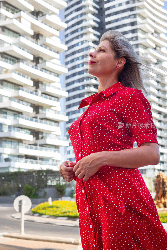 一个穿着红衣服的年轻漂亮女孩站在高楼大厦的背景下