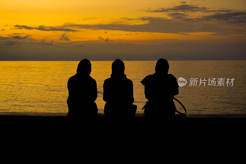 落日背景上悲凉的人，剪影三个女人坐在夕阳下的海滩上