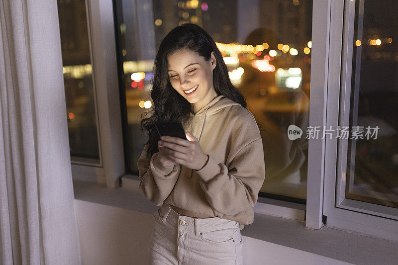 年轻女子在夜间使用智能手机的正面视图，背景是城市景观