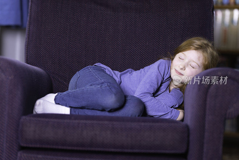 红头发的年轻女孩蜷缩在扶手椅上睡着了