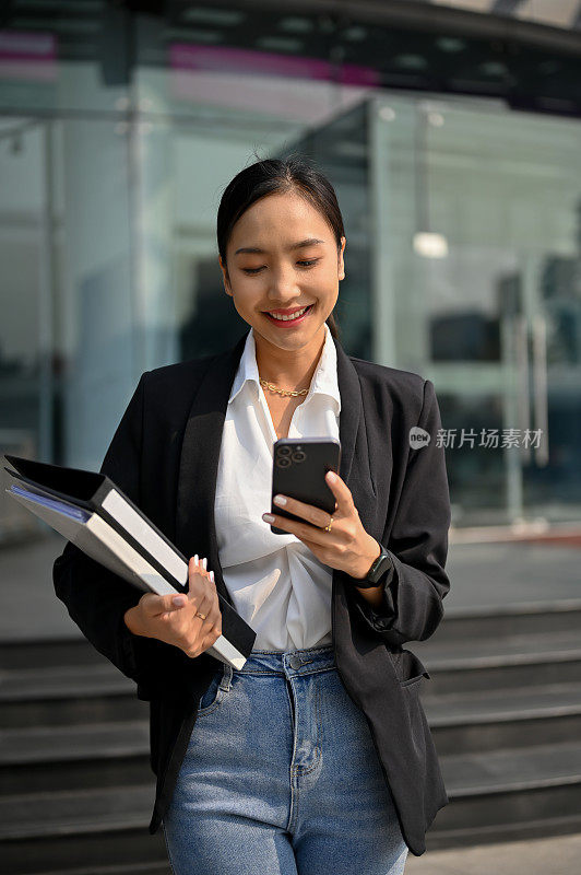 迷人的千禧亚洲女商人在街上走着用她的智能手机