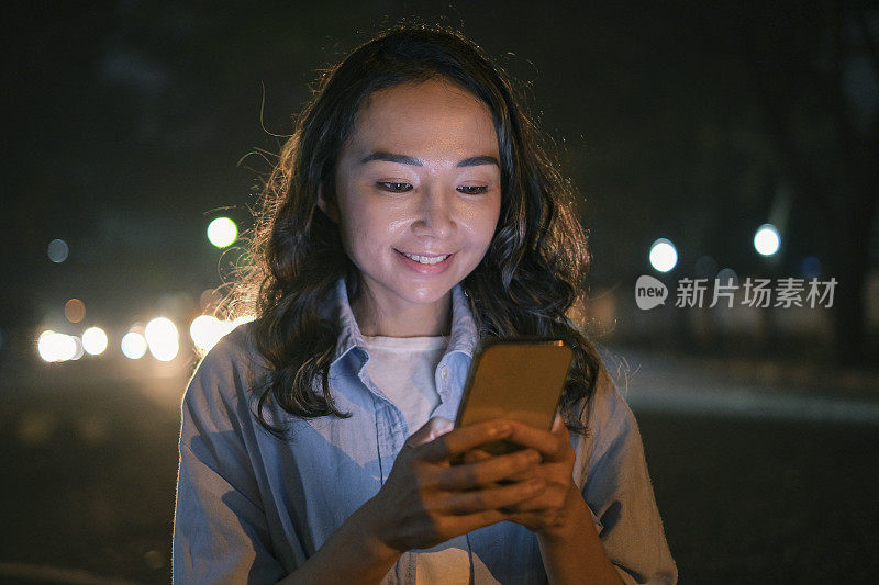 微笑的亚洲妇女在晚上走在街上接受好消息