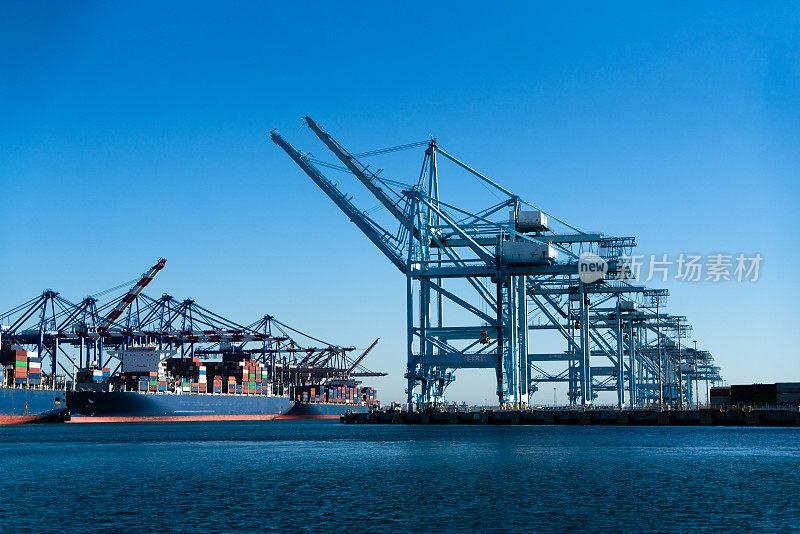 一队巨大的货船挤满了洛杉矶的港口，它们巨大的船体伸向天空。它们满载着集装箱，是全球贸易和互联经济的象征。
