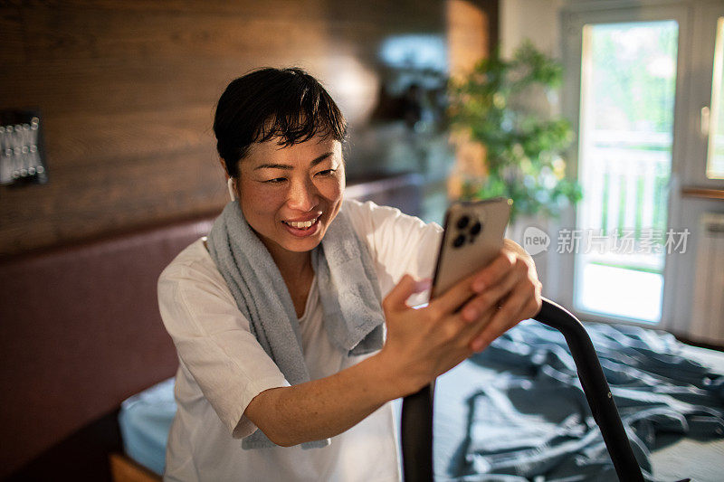 年轻的日本女子一边使用智能手机一边在室内自行车上锻炼