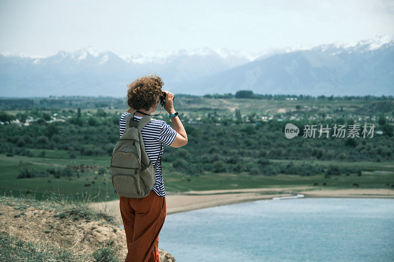 一位女游客站在高高的湖岸上，用双筒望远镜眺望