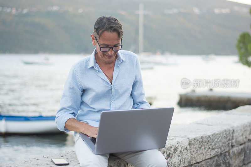 坐在海边用笔记本电脑咨询客户的商人