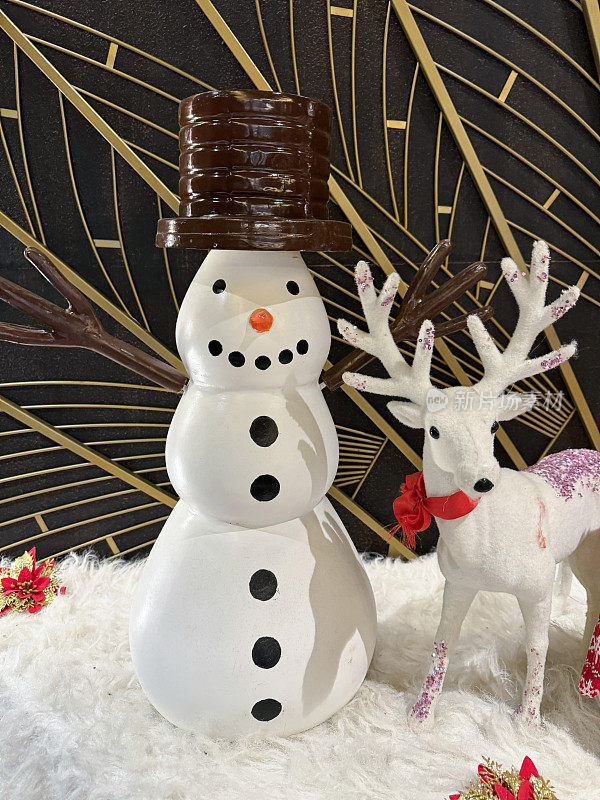 圣诞场景的特写图像，卡通雪人雕像除了驯鹿装饰，人造雪花，金色和黑色的背景，重点在前景