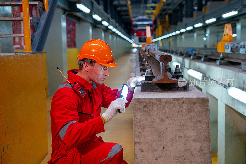 穿着安全制服的专业技术工人手持灯管在工厂工作场所与电气轨道或空轨列车一起工作。