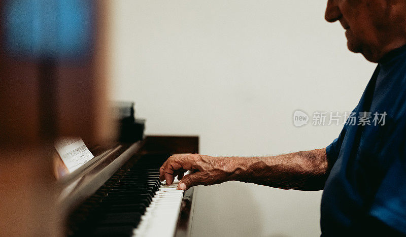 年长的成年男子若有所思地弹奏着一架立式钢琴