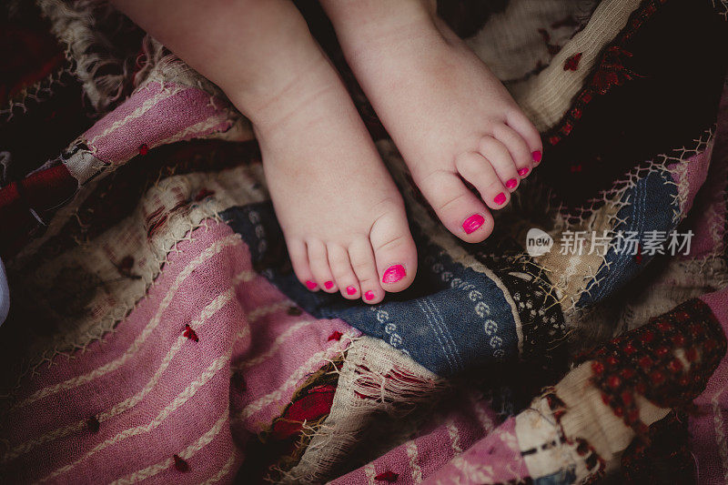 涂着粉红色脚趾甲的小女孩坐在毯子上