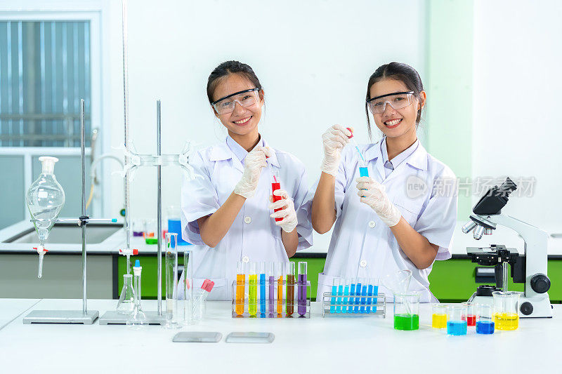 世界卫生组织的两名亚洲女科学家，都是医生，站在生物实验室里，拿着试管和化学品，用于治疗COVID和其他全球科学大流行的疫苗和药物。