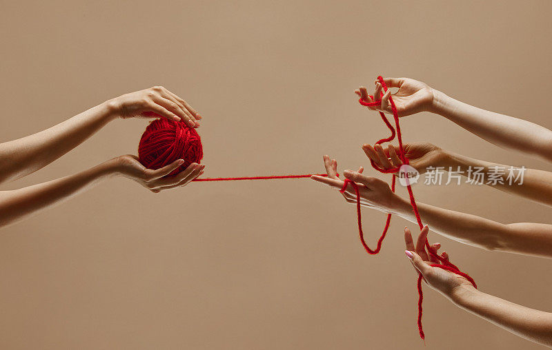 几只手在红色的纱线球上相互作用，拉动和扭转线，象征着关系的复杂性和相互关联性。