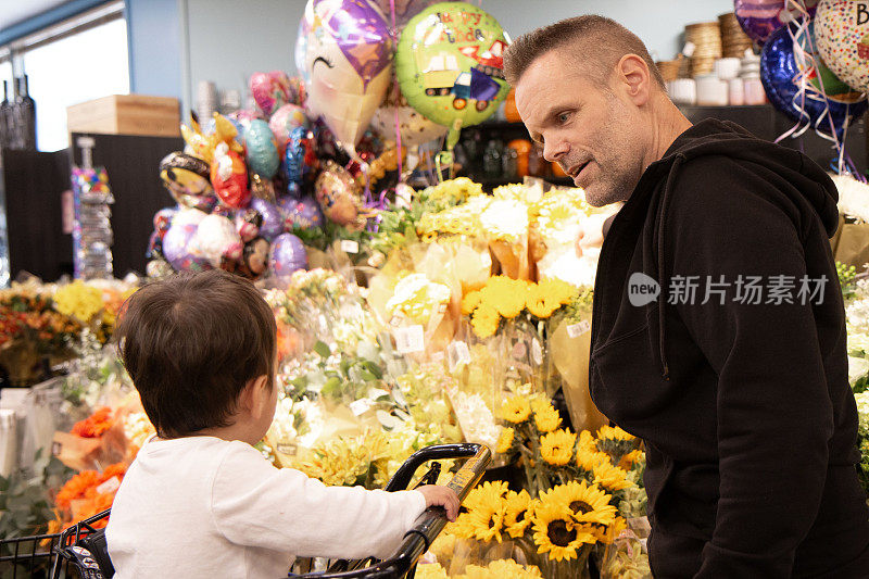 爸爸和蹒跚学步的儿子在杂货店为妈妈挑选鲜花