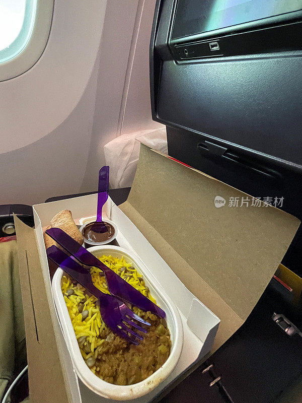飞机折叠桌子的一次性，纸板食物托盘包含印度咖喱饭藏红花饭，面包卷，一次性使用，塑料碗的巧克力慕斯，一次性塑料紫色餐具，上升的观点