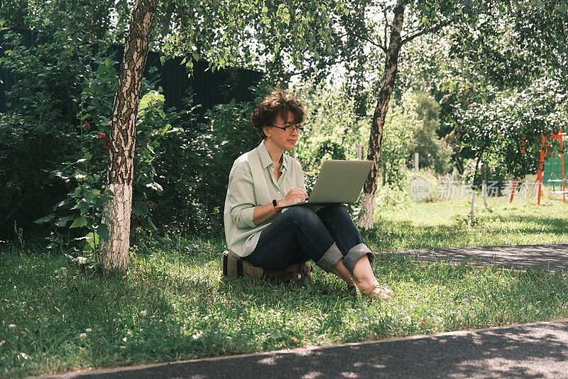 成熟的女人是坐在草地上使用笔记本电脑