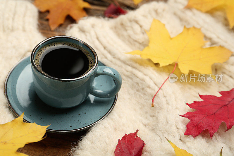 一杯热咖啡，毛衣和秋叶放在桌子上，文字的空间