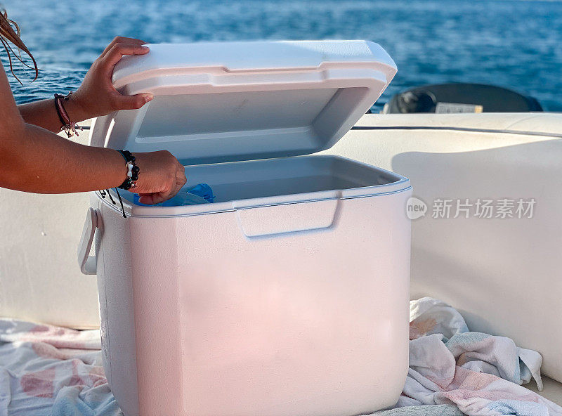 塑料制品与有趣的背景:女孩的手从船上的冷却器中拿饮料