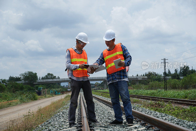 2名亚洲工程师在外面检查修建一条高速铁路。