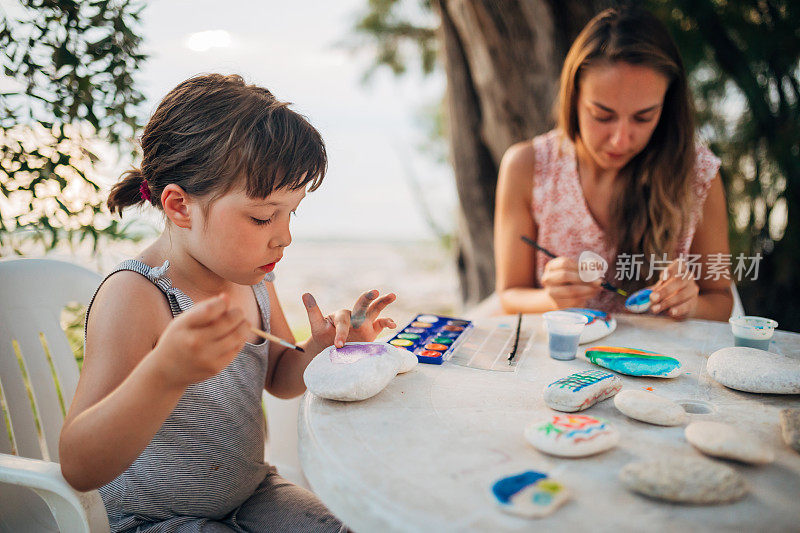 一个女人和她的女儿喜欢画画和涂色，所以他们花了一天的时间在海滩上，在岩石上画画